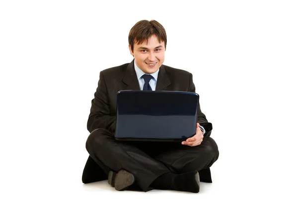 Hombre de negocios sonriente sentado en el suelo y trabajando en el ordenador portátil — Foto de Stock