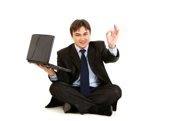 坐在地板上用微笑显示 ok 手势的商人的笔记本电脑 — 图库照片