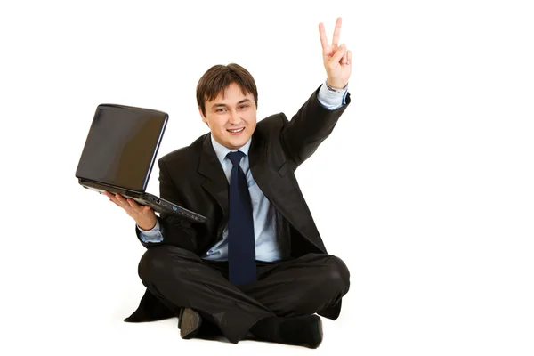 坐在地板上的笔记本电脑微笑商人显示胜利手势 — 图库照片