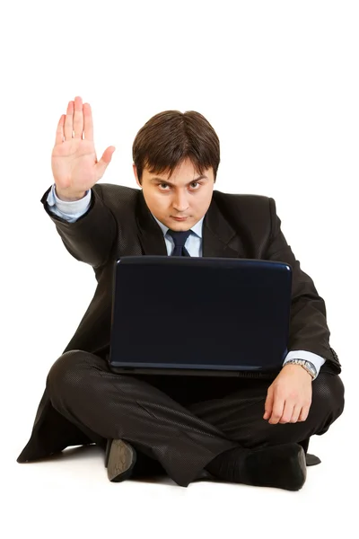 Сидя на полу с ноутбуком серьезный бизнесмен показывает стоп-жест — стоковое фото