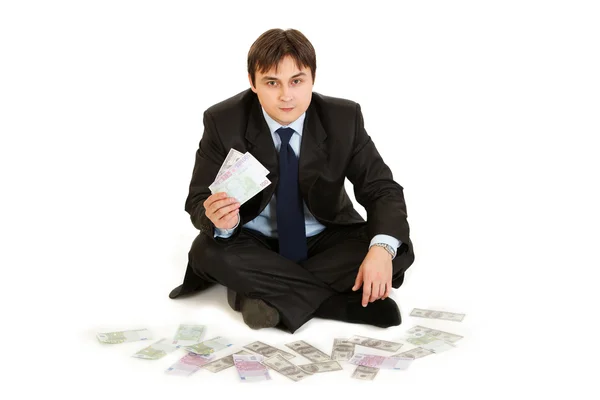 Exitoso hombre de negocios sentado rodeado de dinero y sosteniendo varios bancos —  Fotos de Stock
