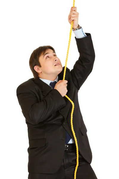 Stubborn young businessman climbing up on rope — Stock Photo, Image