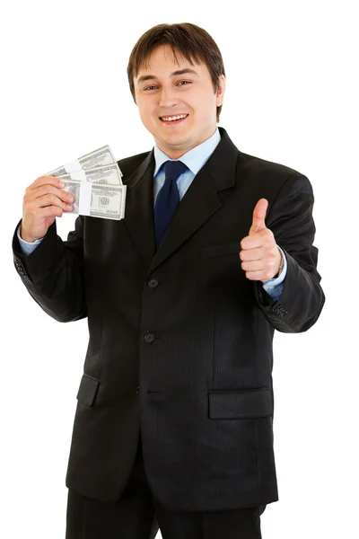 Pleased modern businessman holding stack of dollars and showing thumb up ge — Stock Photo, Image
