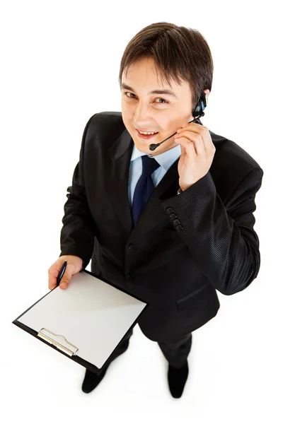 Sonriente joven hombre de negocios con auriculares sujetando portapapeles — Foto de Stock