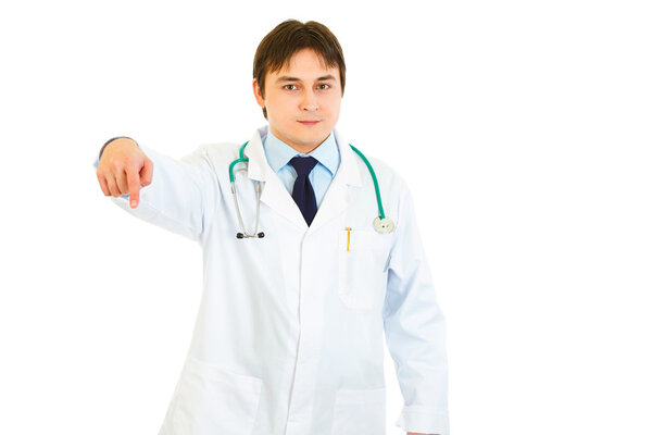 Smiling young medical doctor pointing finger down isolated on white