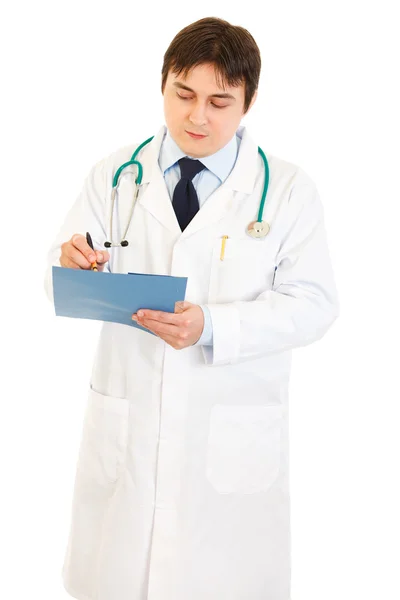Seriöser Arzt mit Stethoskop, der Notizen in medizinischer Tabelle macht — Stockfoto