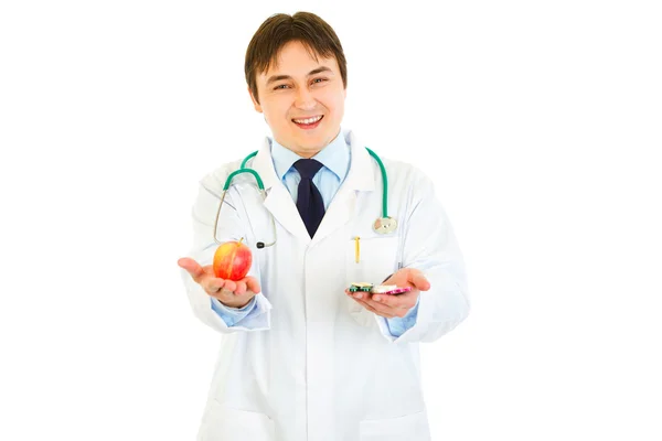 Улыбающийся врач с таблетками в одной руке и яблоко в другой — стоковое фото