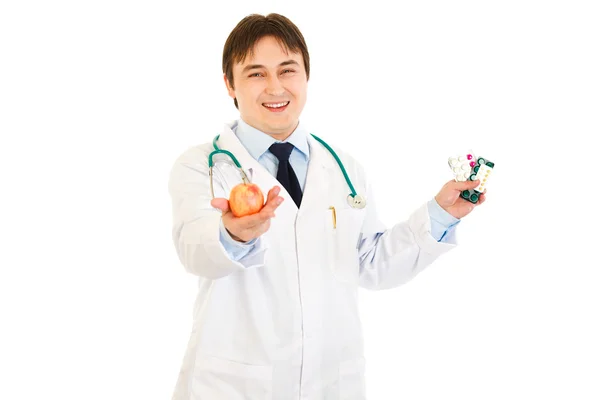 Médico sonriente dando manzana y sosteniendo paquetes de pastillas en otro han —  Fotos de Stock