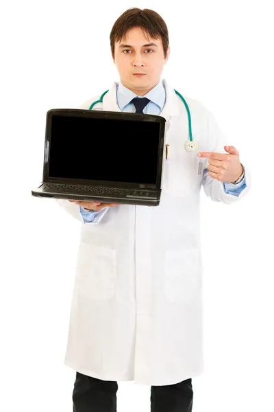 Seriöser Arzt zeigt mit dem Finger auf Laptops leeren Bildschirm — Stockfoto