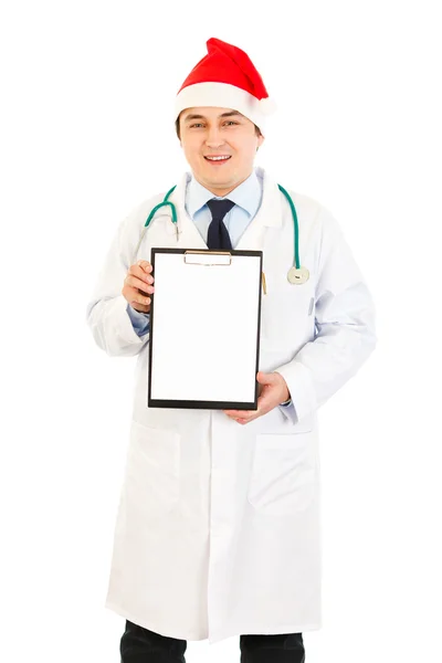 Médico sonriente en Santa Sombrero sosteniendo portapapeles en blanco — Foto de Stock