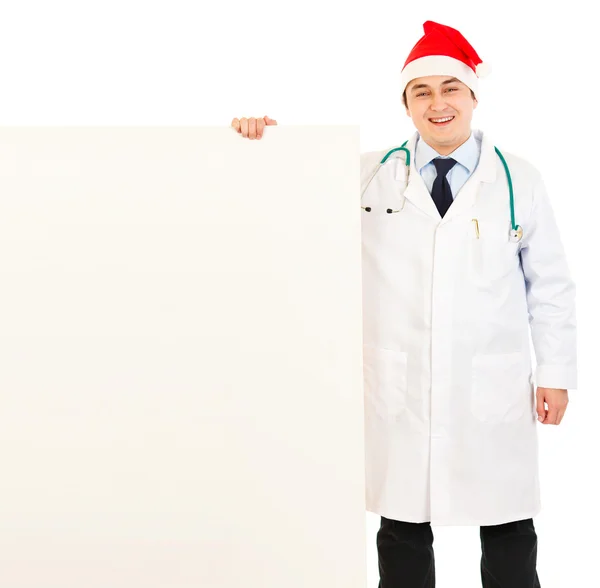 산타 모자 빈 게시판을 들고 있는 의사 웃 고 — 스톡 사진