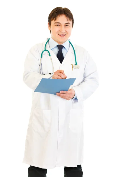 Smiling medical doctor writing report in medical chart of patient — Stock Photo, Image
