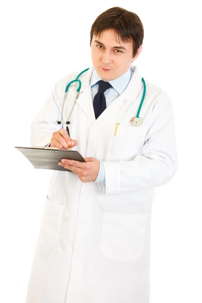 Smiling doctor with stethoscope making notes in medical chart Royalty Free Stock Images