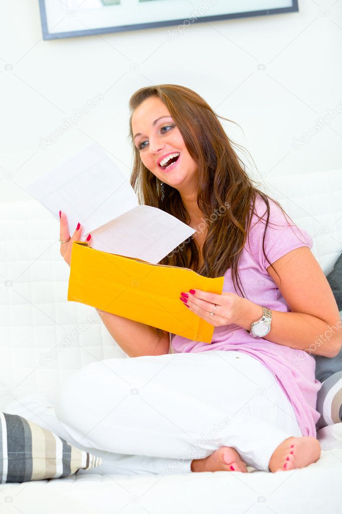 Happy pretty woman sitting on sofa and reading letter