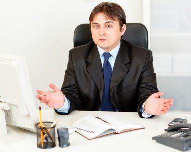 Confused modern businessman sitting at office desk clipart