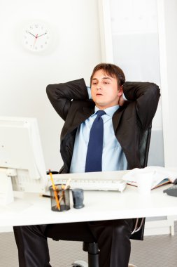 Tired businessman sitting at office desk and looking at computer monitor. clipart