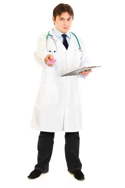 Médico serio sosteniendo portapapeles y medicamentos recetados en manos aisladas o —  Fotos de Stock