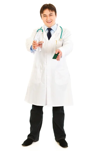 Улыбающийся врач держит в руках упаковку таблеток и стакан воды — стоковое фото