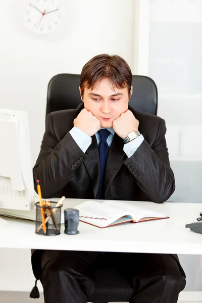 Проницательный бизнесмен сидит за рабочим столом и держит голову на руках — стоковое фото