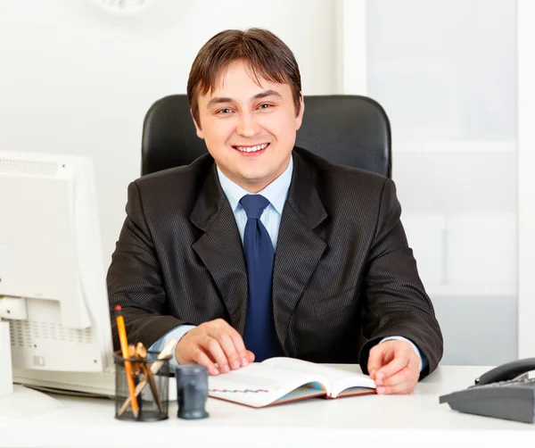 オフィスの机に座って近代的なビジネスマンの笑みを浮かべてください。 — ストック写真