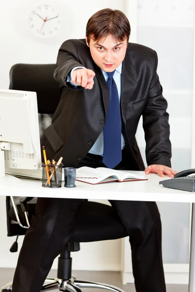 怒っている近代的な実業家のオフィスの机に立っていると指を指すのよ — ストック写真