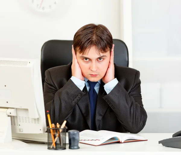 Modern businessman sitting at office desk and making hear no evil gesture — Stock Photo, Image