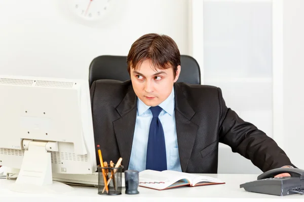 Предупредите современного бизнесмена, сидящего за столом офиса и смотрящего в угол — стоковое фото