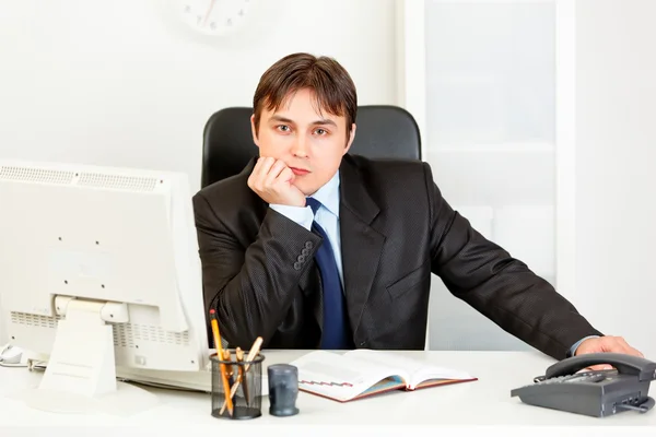 Задумчивый элегантный бизнесмен сидит за столом офиса — стоковое фото