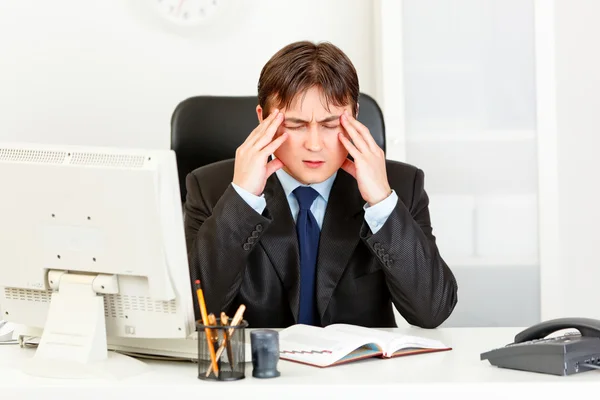 Empresário com dor de cabeça sentado na mesa do escritório e de mãos dadas na cabeça — Fotografia de Stock