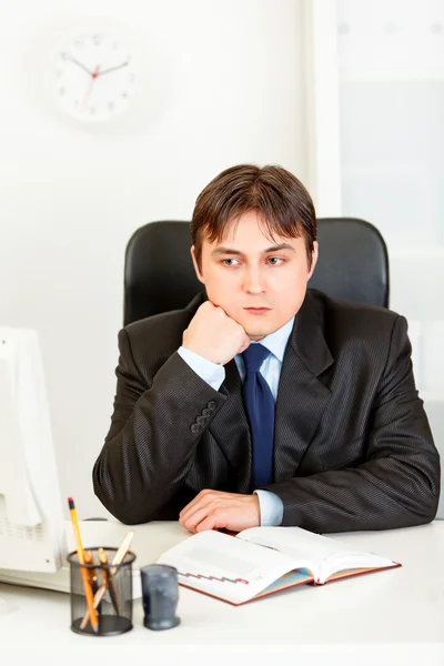 Empresário pensativo sentado na mesa do escritório e manter a cabeça na mão — Fotografia de Stock