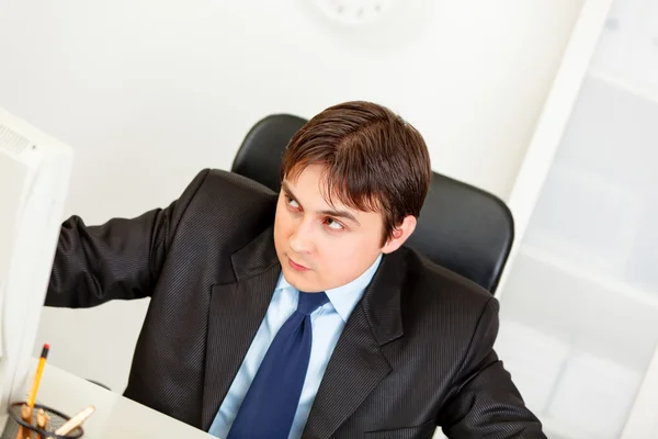 Alerte o empresário moderno sentado na mesa de escritório e olhando no canto — Fotografia de Stock