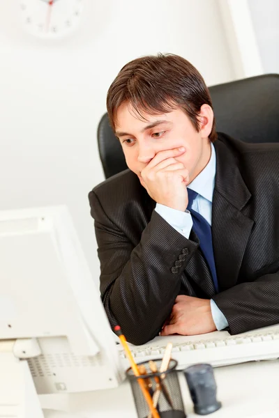 Fundersam affärsman sitter på kontoret skrivbordet och tittar på datorskärmen — Stockfoto
