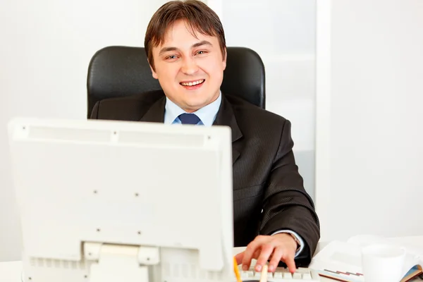 Hombre de negocios sonriente sentado en el escritorio de la oficina y trabajando en PC — Foto de Stock