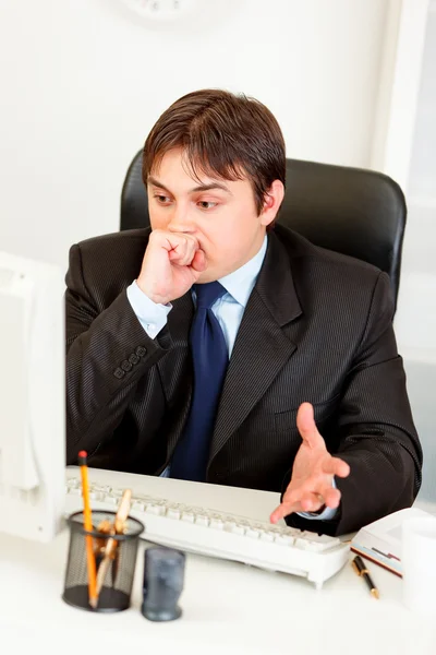 Förvirrad affärsman sitter vid office skrivbord och förvånansvärt tittar på com — Stockfoto