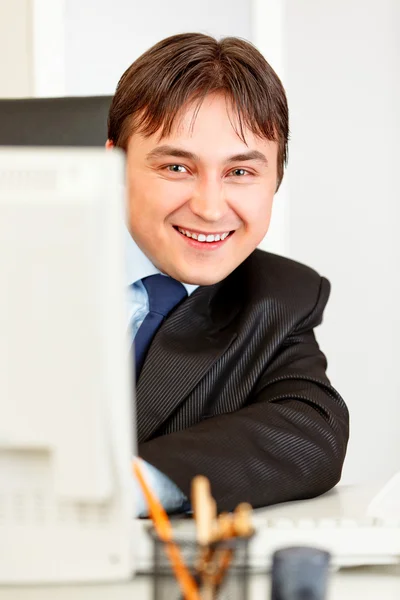 Mosolyogva ül íróasztal és a számítógép látszó modern üzletember — Stock Fotó