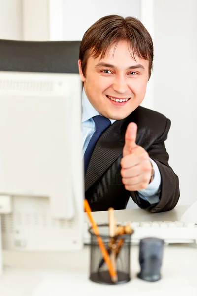 Empresário sorridente olhando de monitor e mostrando polegares acima gesto — Fotografia de Stock
