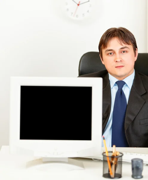 Homem de negócios moderno sentado na mesa de escritório e mostrando monitores tela em branco — Fotografia de Stock