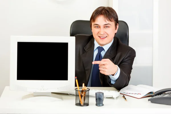 Biznesmen uśmiechający się siedząc w biurze informacji turystycznej i wskazując palcem na monitor — Zdjęcie stockowe