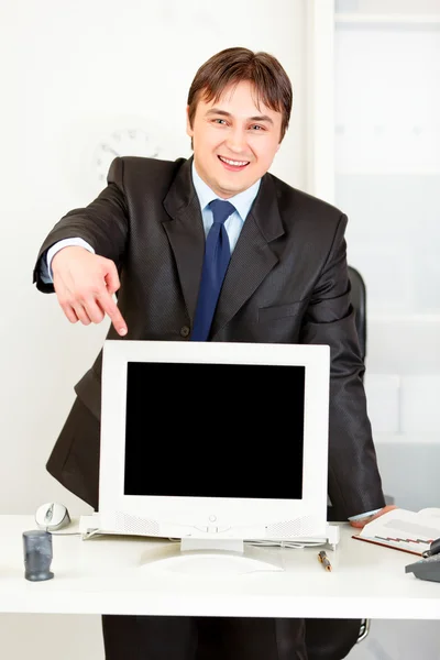 Uomo d'affari sorridente in piedi dietro la scrivania dell'ufficio e puntare il dito contro mo — Foto Stock