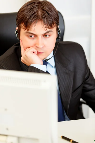Komoly üzletember és ül íróasztal, és nézi m fülhallgató — Stock Fotó