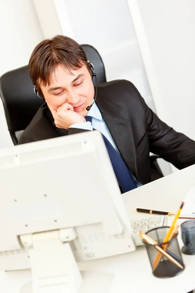 Sonriente hombre de negocios moderno sentado en el escritorio de la oficina y hablando en auriculares — Foto de Stock