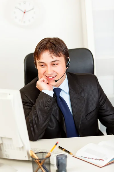 Hombre de negocios sonriente con auriculares sentado en el escritorio de la oficina y mirando co — Foto de Stock