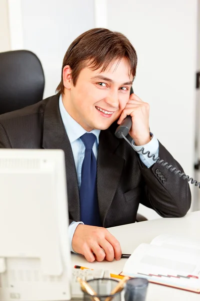 Vänliga moderna affärsman sitter vid office skrivbord och prata telefon — Stockfoto