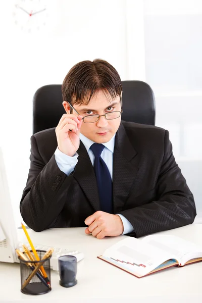 Empresário autorizado sentado na mesa do escritório e endireitando os óculos — Fotografia de Stock