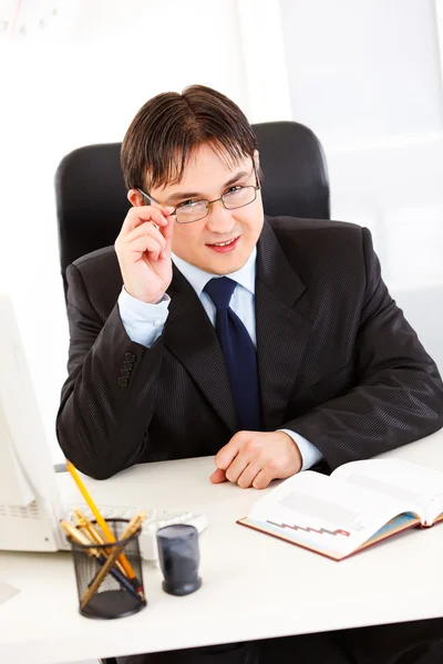Uomo d'affari sorridente seduto alla scrivania dell'ufficio e occhiali raddrizzanti — Foto Stock