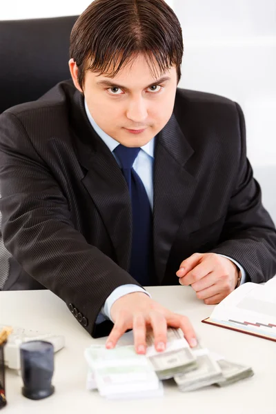 Концентрированный бизнесмен, сидящий за столом офиса и раздающий денежные пакеты — стоковое фото