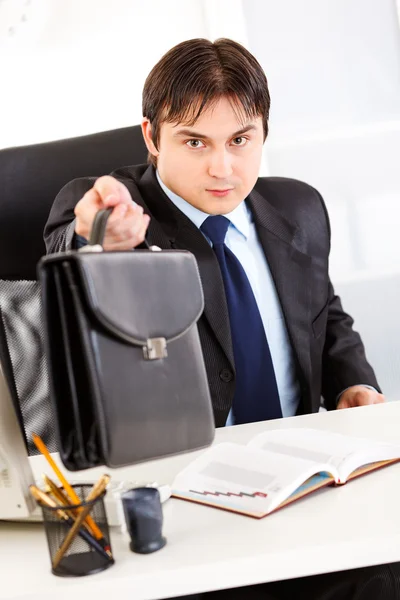 Hombre de negocios atento sentado en el escritorio de la oficina y dando maletín — Foto de Stock