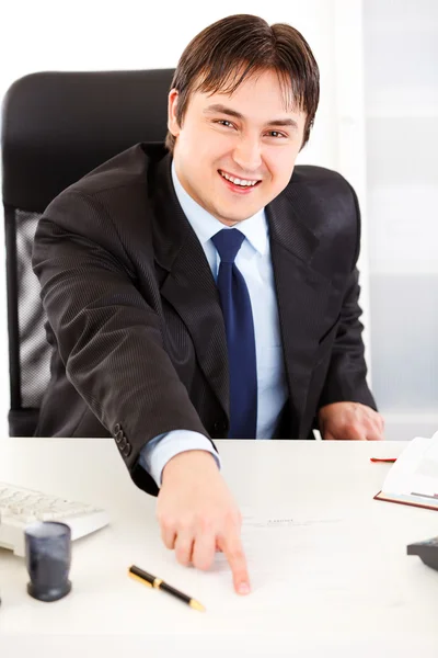 Sonriente hombre de negocios sentado en el escritorio de la oficina y señalando en el documento para si — Foto de Stock