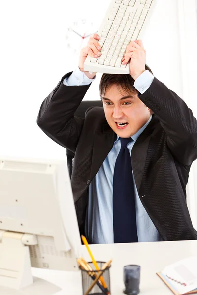 Homem de negócios irritado sentado na mesa do escritório e destruindo o computador usando a chave — Fotografia de Stock