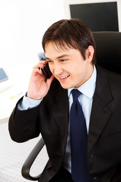 Jovem empresário sorridente falando por telefone no escritório — Fotografia de Stock